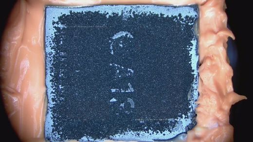 02 · Progressive removal — Encapsulant removal has begun; the dies remain covered.